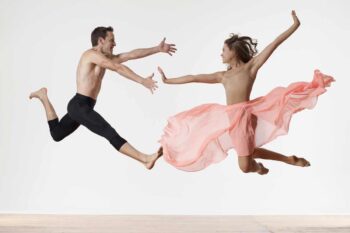 Two dancers leaping toward each other, the woman trailing pink chiffon