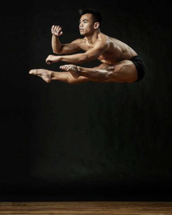Male dancer in a split leap against a black backdrop
