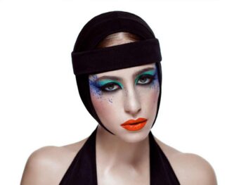 Model in a black headwrap with blue and green eye makeup and orange lips