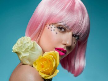Model in a pink bob wig with star face gems, holding yellow roses