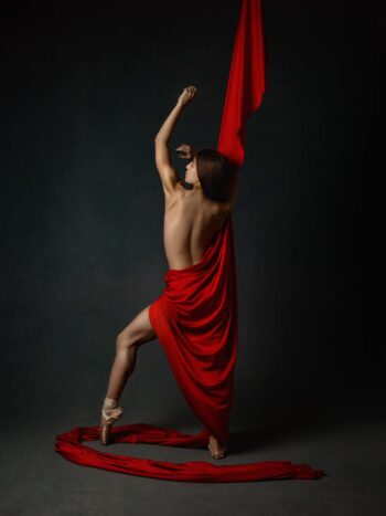 Dancer posing with flowing red fabric against a dark background