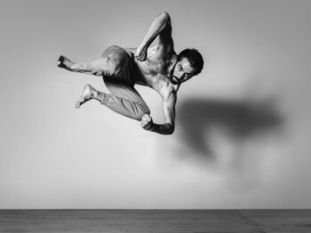 Male dancer mid-air in a tucked leap, black-and-white studio photograph